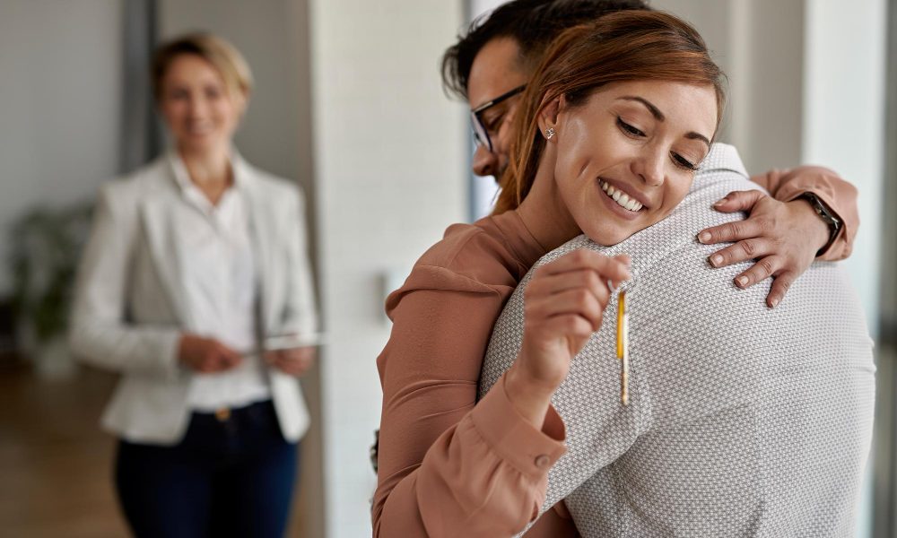 Sıfır ev alırken dikkat edilmesi gerekenler: yeni dairenin anahtarını teslim alan mutlu çift ve emlak danışmanı